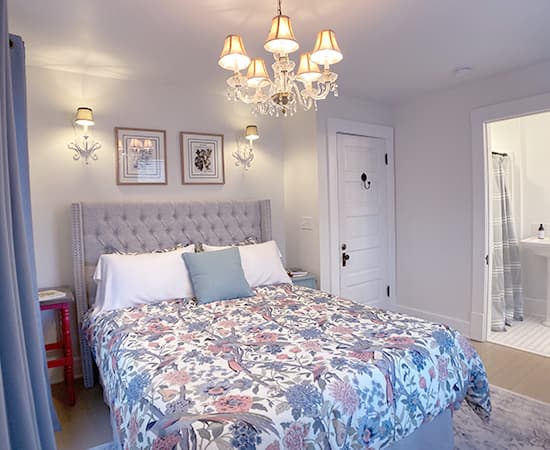 An elegant bedroom featuring a tufted grey wingback headboard, floral patterned bedding in blue and coral, and a sparkling crystal chandelier centered above the bed.