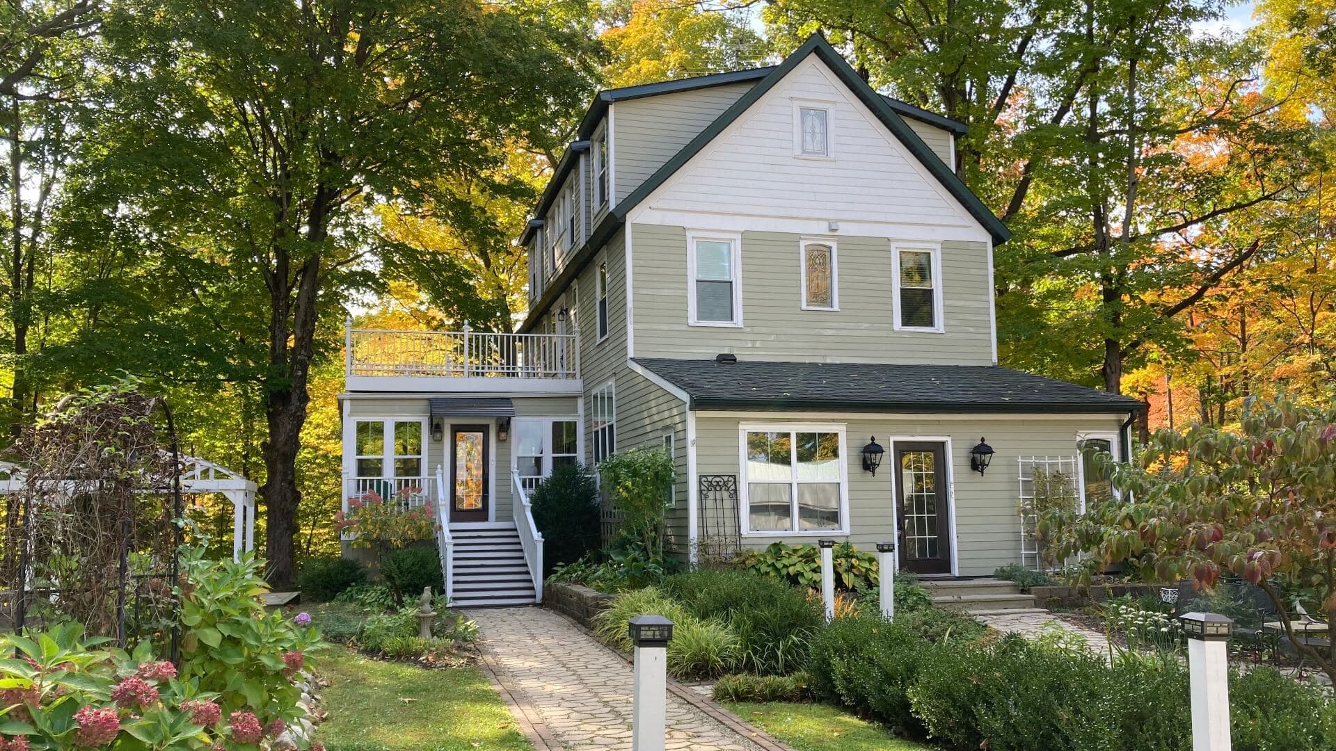 A two-story house with a porch, surrounded by greenery and autumn-colored trees.
