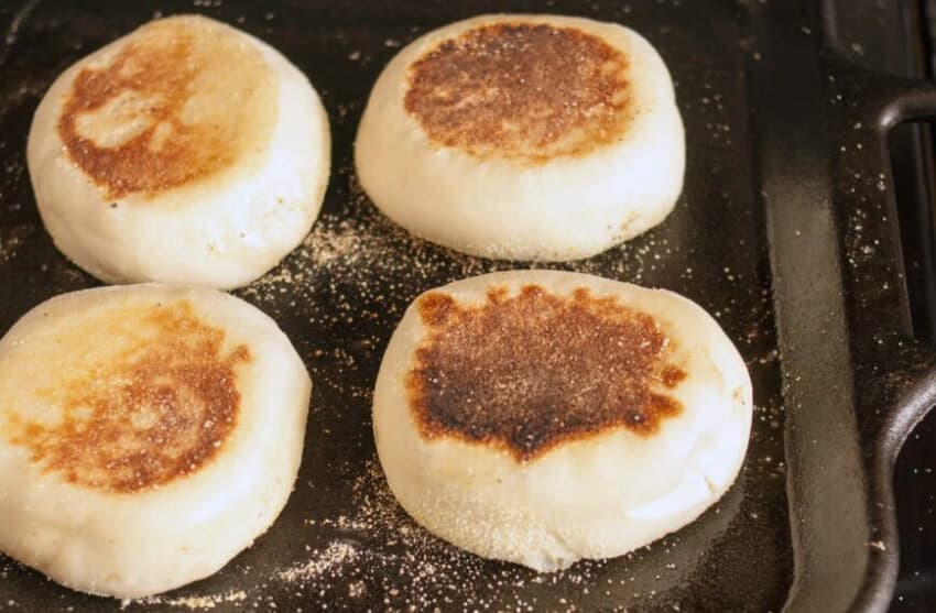 Four toasted English muffins on a griddle sprinkled with flour.