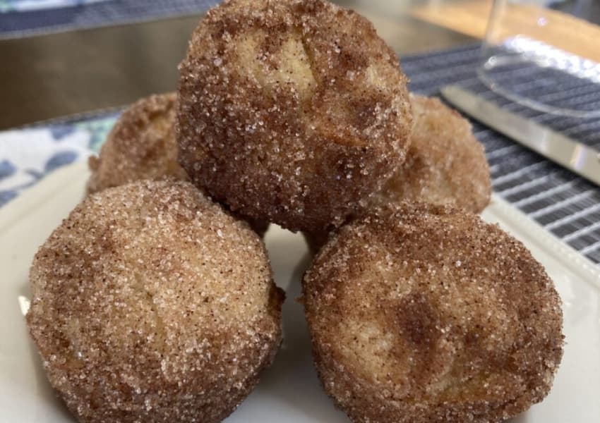 A plate of golden, cinnamon-sugar coated doughnut holes stacked together.
