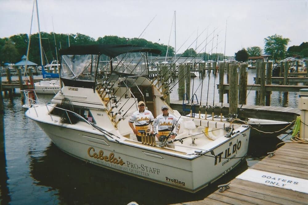 Two fishermen pose on a fishing boat docked at a marina.