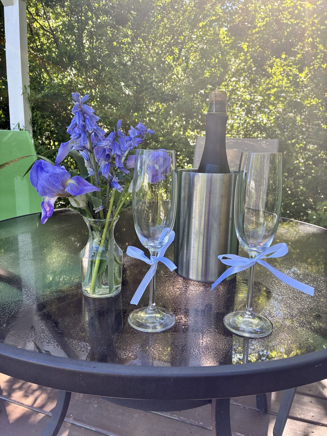 A table set with champagne flutes, a bottle of champagne, and a vase of blue flowers.