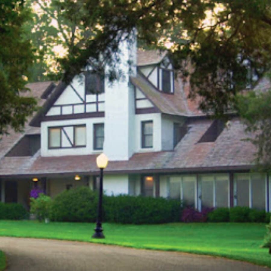 A large, two-story house with a mix of architectural styles, surrounded by green lawns and trees.