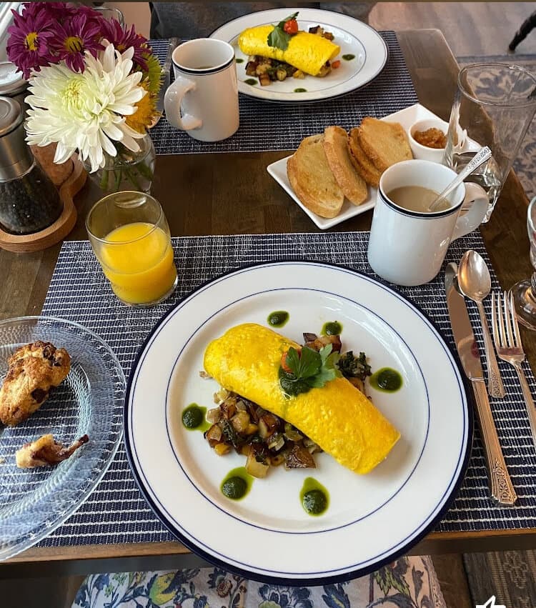 A colorful breakfast spread featuring an omelet, sautéed vegetables, toast, and drinks on a textured table setting.