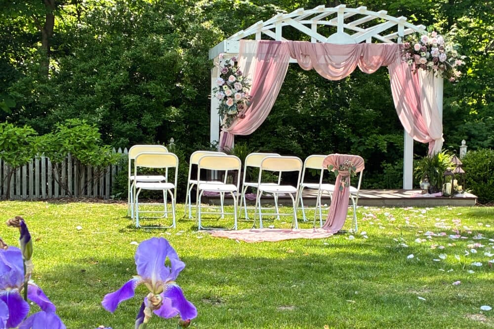 A floral-decorated wedding arbor with white chairs set up in a grassy area.