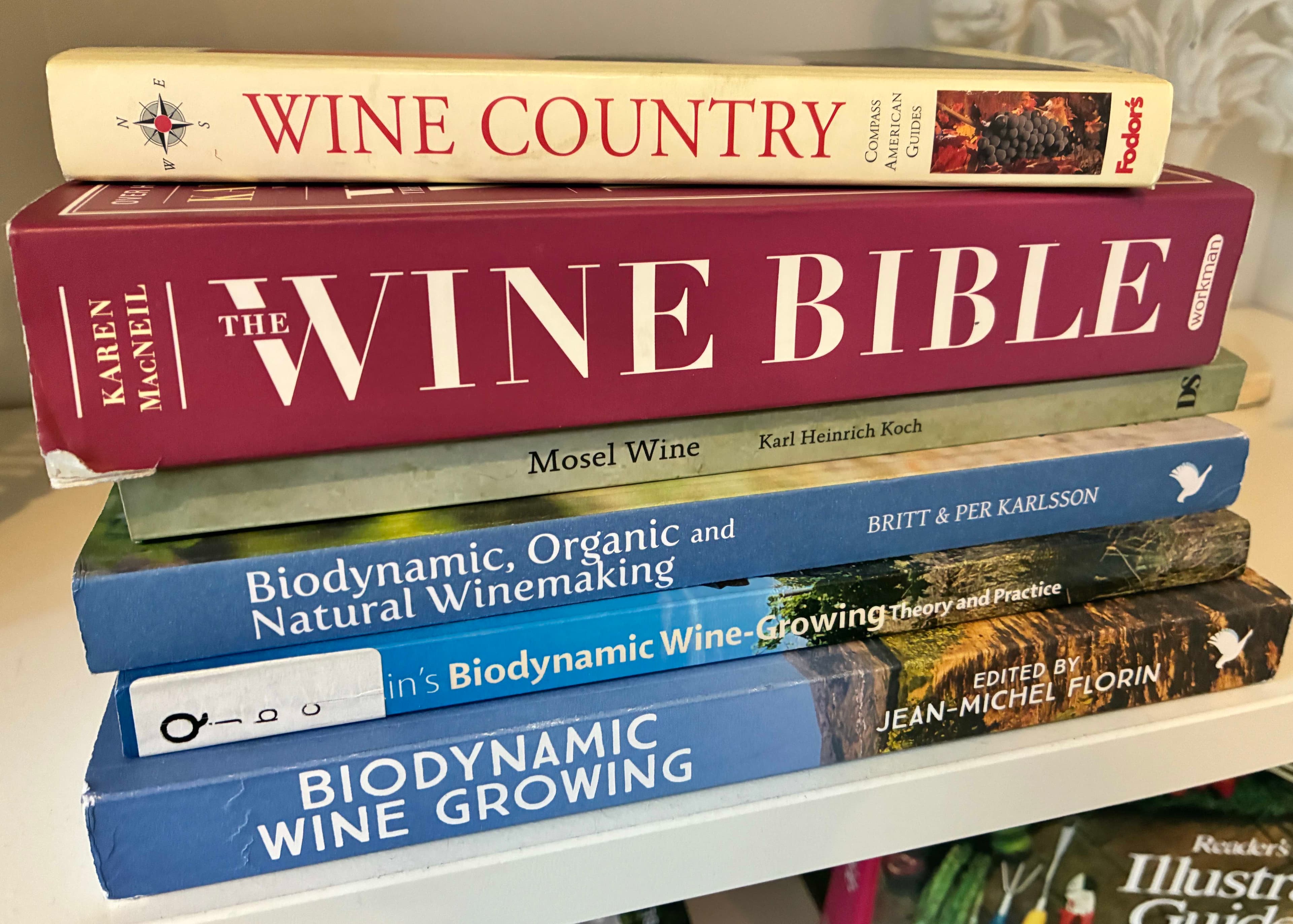 A stack of wine-related books, including "The Wine Bible" and "Biodynamic Wine Growing."