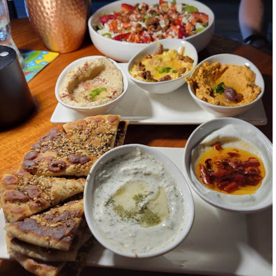 A platter featuring various dips, flatbread, and a colorful salad.