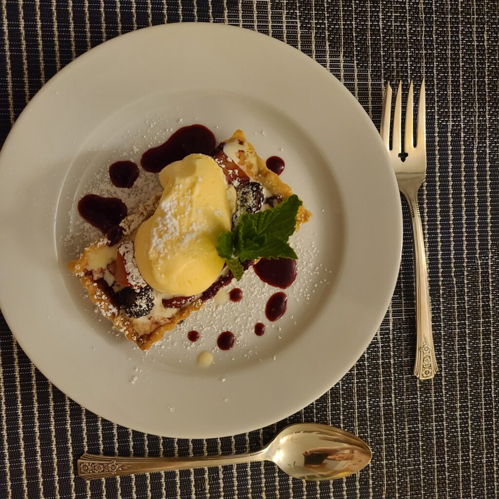 Dessert with ice cream and raspberry sauce swirled on a white plate with antique silverware
